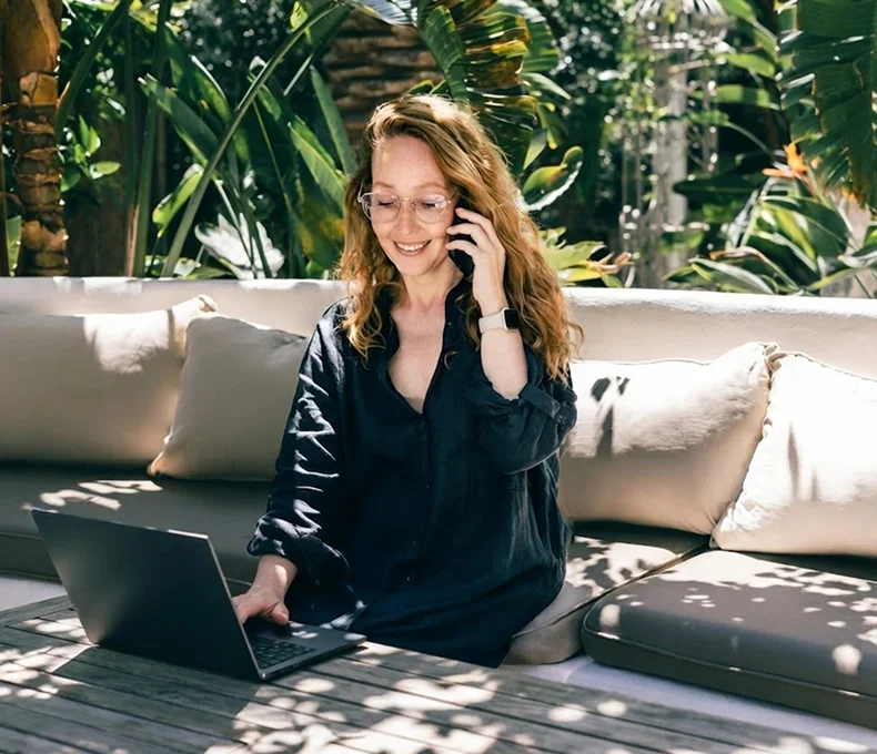Woman working on a laptop while talking on the phone outdoors